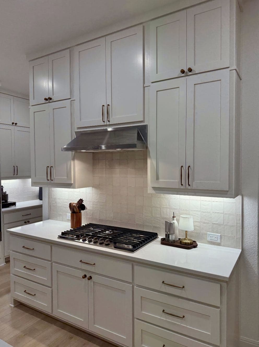 A cream square-tile kitchen backsplash running behind a gas cooktop and stainless hood